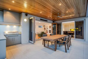 Cuina moderna amb sostre de fusta, zona de menjador amb taula i cadires de fusta, i una porta corredissa de vidre que dona a un espai saló.