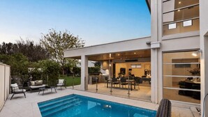 A modern outdoor pool area with a covered patio, seating, and a view of the interior. - The Anchorage on Henley (Charles Sturt)