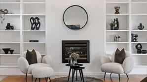 A modern living room with white shelving, a fireplace, two armchairs, and a round mirror. - The Anchorage on Henley (Charles Sturt)