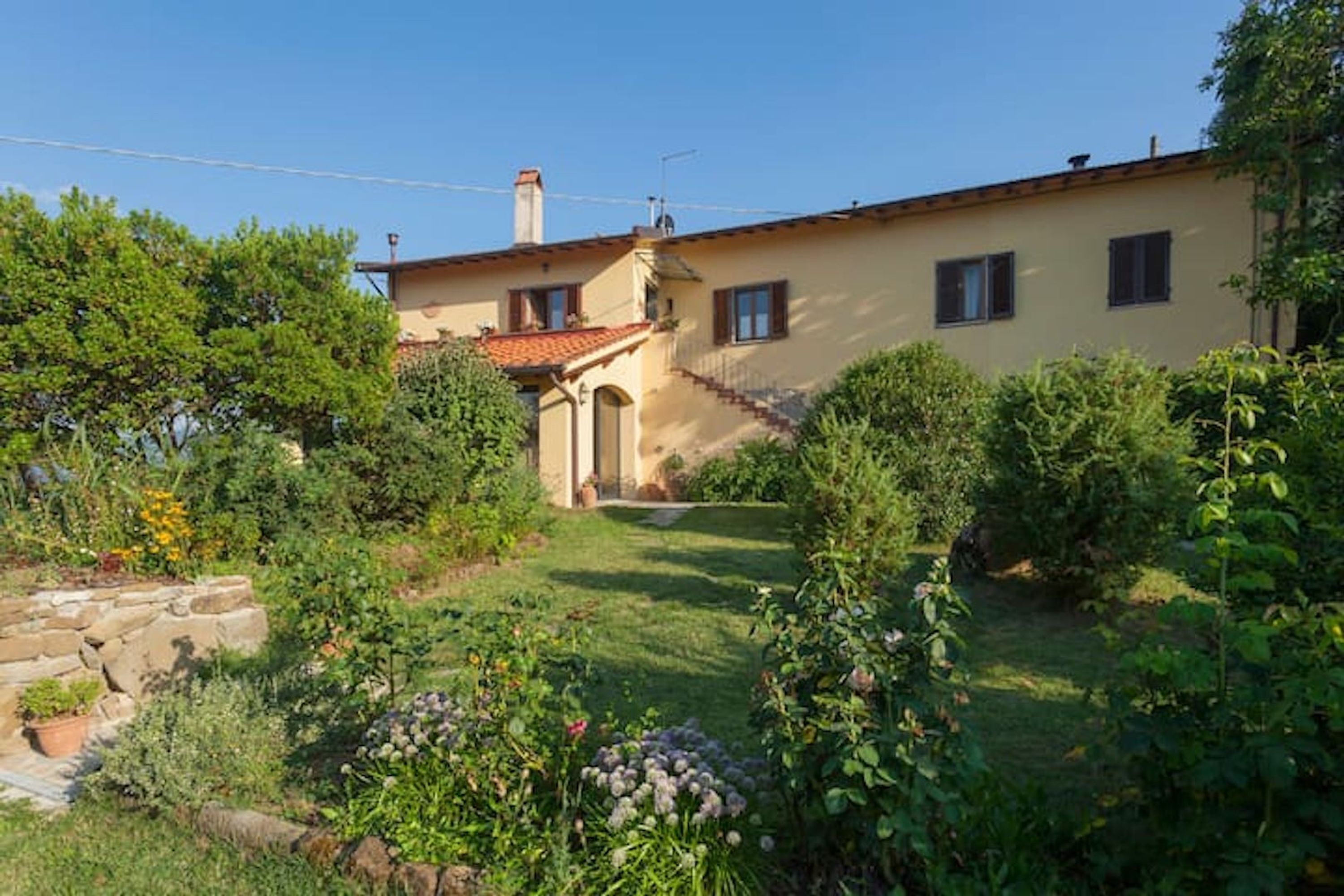 A two-story house with a garden, a stone wall, and a clear sky.