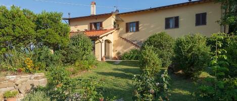A two-story house with a garden, a stone wall, and a clear sky.