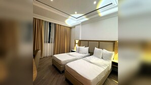 Habitación de hotel con dos camas, un ventanal con cortinas, suelo de madera y un diseño moderno en el techo.
