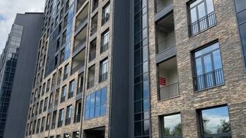 Un edificio residencial de varios pisos con un diseño arquitectónico moderno, que cuenta con balcones, ventanas amplias y un sendero pavimentado con un banco.