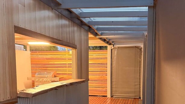 A covered outdoor area with a wooden deck, a metal railing, and a glass enclosure.