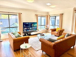 A living room with two sofas, a coffee table, and a flat-screen TV. - Luxury 5BR+5Bath Home •Style, Space & Comfort • EV (Truganina)