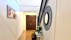Un pasillo con suelo de madera, un banco, una mesa con plantas y una puerta al final.
