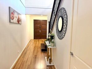 A hallway with wooden flooring, a bench, a table with plants, and a door at the end. - Luxury 5BR+5Bath Home •Style, Space & Comfort • EV (Truganina)