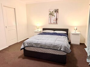 A bedroom with a bed, two bedside tables, a door, and a wall-mounted picture. - Luxury 5BR+5Bath Home •Style, Space & Comfort • EV (Truganina)