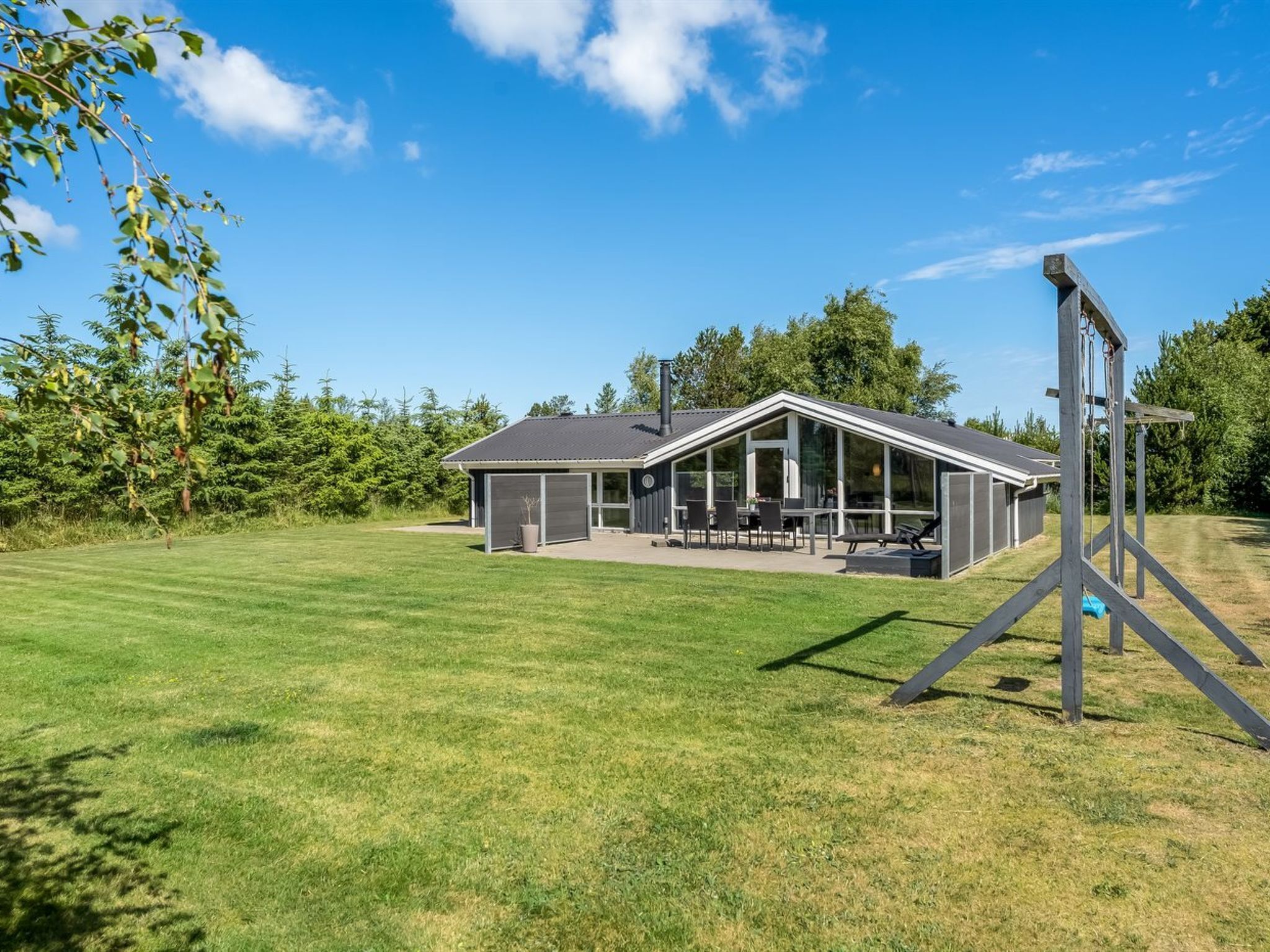 Ett modernt hus med en stor uteplats, ett garage och en gungställning i trä.