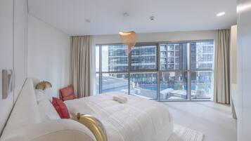 A modern hotel room with a large bed, a view of a swimming pool, and a cityscape through large windows.