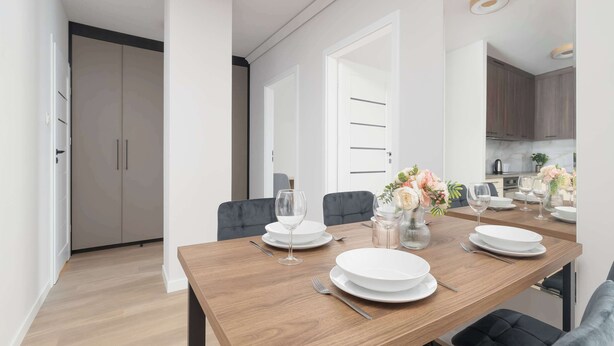 Een eetgedeelte met een houten tafel voor vier personen, stoelen en een vaas met bloemen.