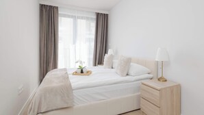 Een slaapkamer met een bed, nachtkastje, lamp en gordijnen.