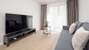 Een moderne woonkamer met een flatscreen-tv, een grijze bank en een klein bijzettafeltje met een plant.