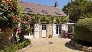 A stone building with a tiled roof, white doors, and a gravel patio with a table and chairs. - La Maison des Roses - A charming house with a garden (Rully)