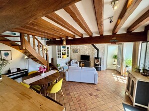 Ein rustikales Interieur mit freiliegenden Holzbalken, einem Essbereich mit einem Klavier, einem Wohnzimmer mit einer Couch und einer Steinwand.
