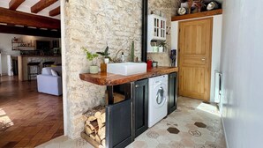A rustic kitchen with a stone wall, wooden beams, a built-in washing machine, and a wooden counter. - La Maison des Roses - A charming house with a garden (Rully)