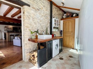 Eine rustikale Küche mit Steinwand, Holzbalken, einer integrierten Waschmaschine und einer Holzausstattung.