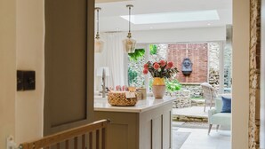 A modern kitchen with a central island, a stone wall, and a seating area with a chair and a table. - Beautiful Cottage in Cirencester Centre (Cirencester)