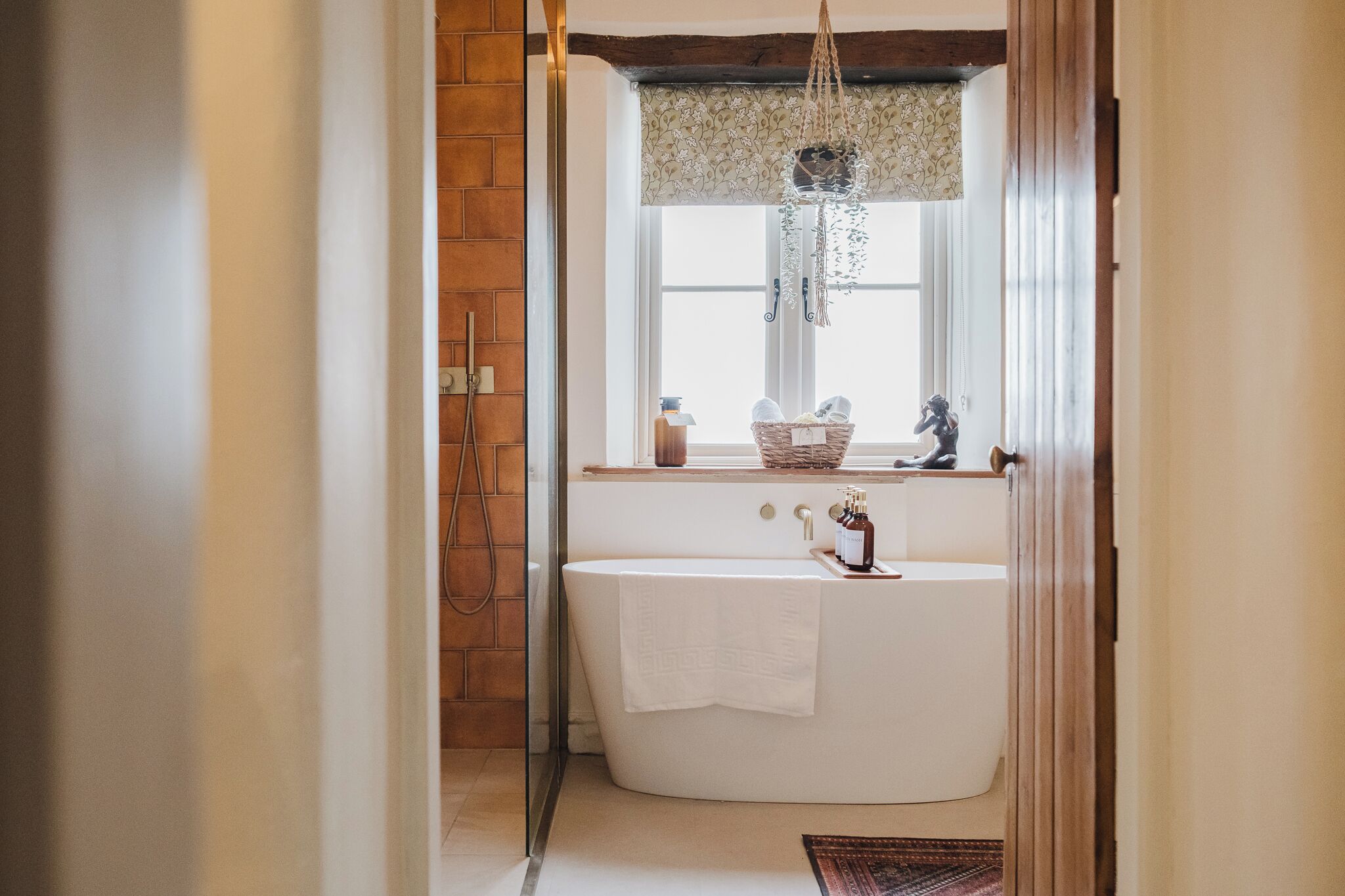 A bathroom with a freestanding bathtub, a window with a decorative valance, and a hanging macrame light fixture.