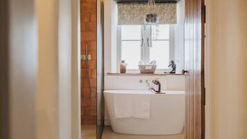 A bathroom with a freestanding bathtub, a window with a decorative valance, and a hanging macrame light fixture.