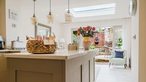 A modern kitchen with a central island, pendant lights, a large window, and a view of the outdoor patio. - Beautiful Cottage in Cirencester Centre (Cirencester)