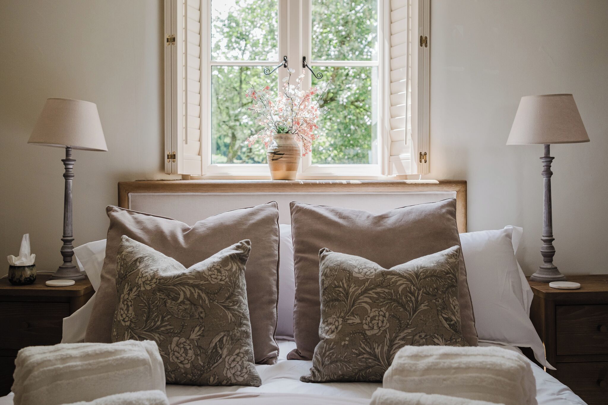A bedroom with a bed, two nightstands, a window with a view of trees, and a vase with flowers.