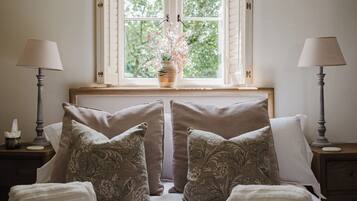 A bedroom with a bed, two nightstands, a window with a view of trees, and a vase with flowers.