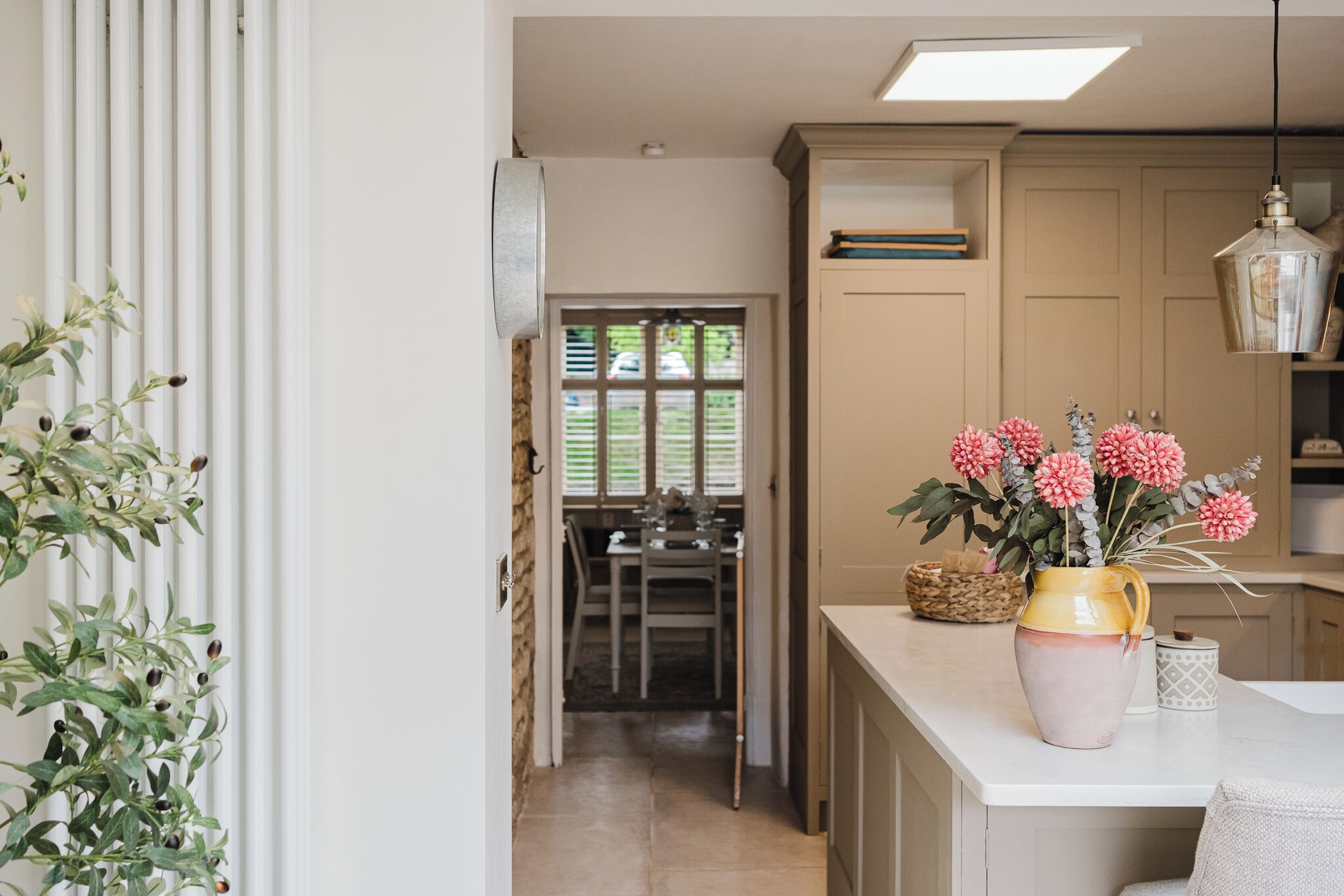 A kitchen with a white countertop, a vase with flowers, and a hanging light fixture.