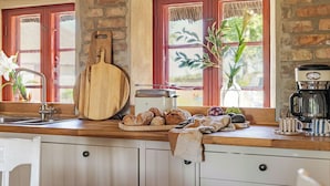 A kitchen with a wooden countertop, a bread basket, a coffee maker, and a window with a view of greenery.