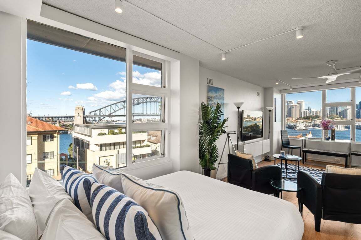 A modern hotel room with a large bed, a desk, and a view of a cityscape and bridge.
