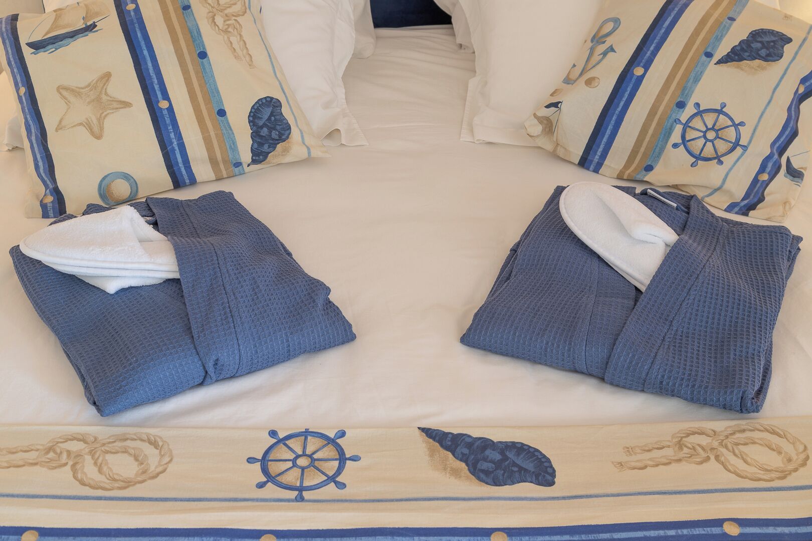 A bed with two pillows, a blanket, and a bedspread with nautical designs.