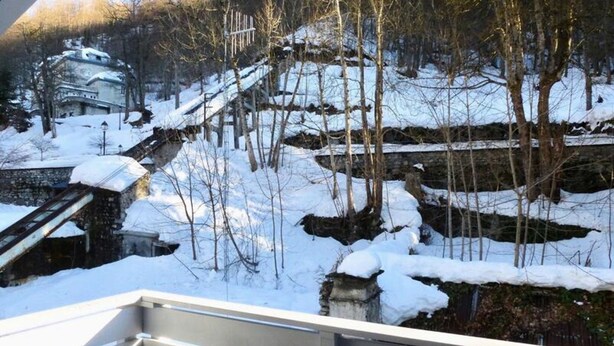 A snow-covered landscape with a stone bridge, bare trees, and a building with a sloped roof. - Oustal Residence for Eight People (Bareges)