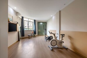 Habitación de hotel con un ventanal grande, una caminadora, una bicicleta estática, una mesita con una silla y un televisor de pantalla plana montado en la pared.