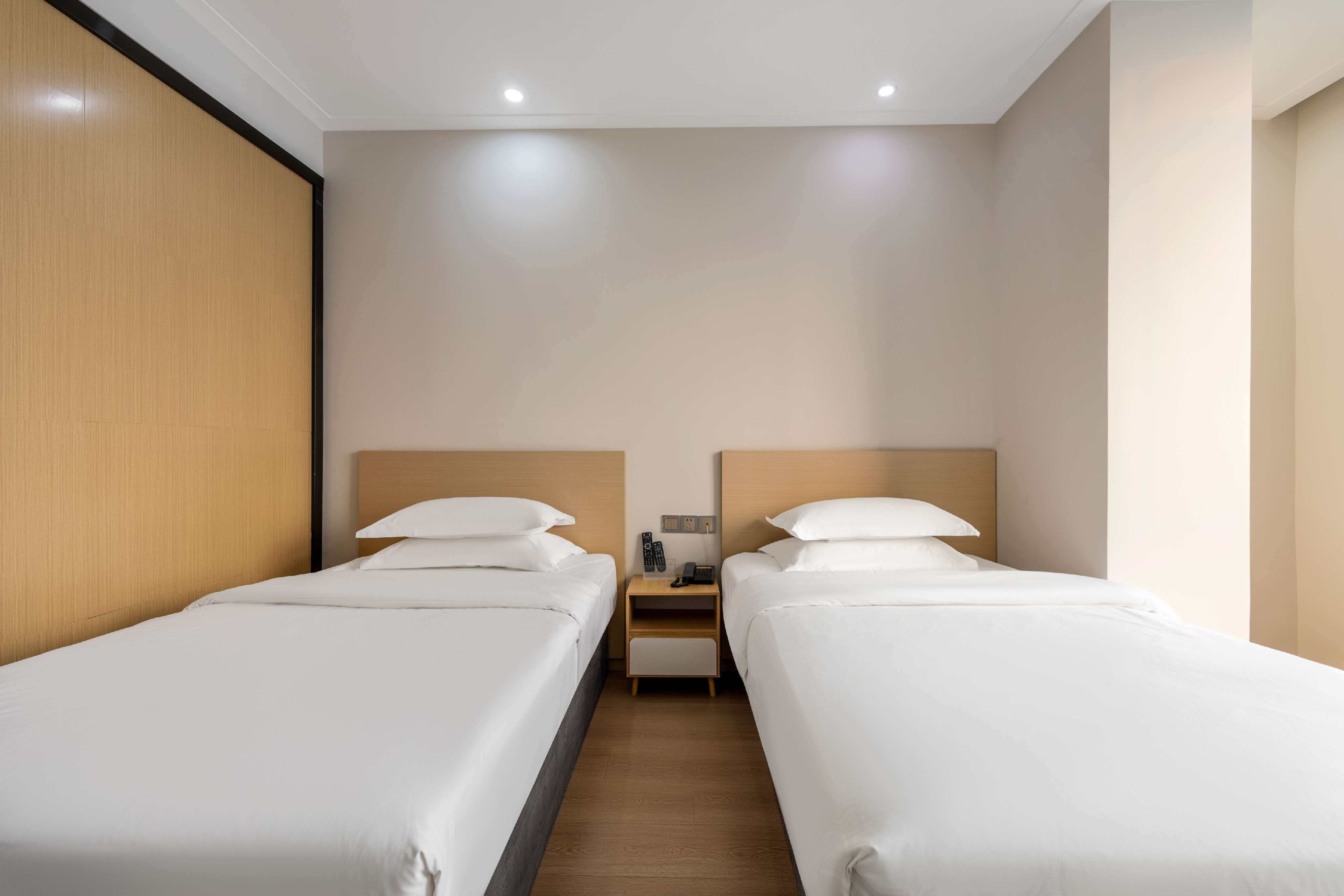 Quarto de hotel com duas camas de solteiro, cabeceira de madeira, mesa de cabeceira com telefone e controles remotos, e piso de madeira.