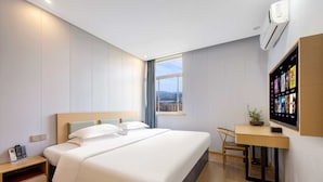 A hotel room with a bed, desk, chair, and a TV on the wall.