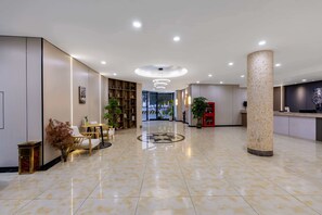 Un vestíbulo amplio con una zona de estar central, un mostrador de recepción y una columna decorativa de gran tamaño.