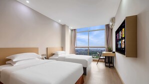 A hotel room with two beds, a desk, a TV, and a large window with a city view.