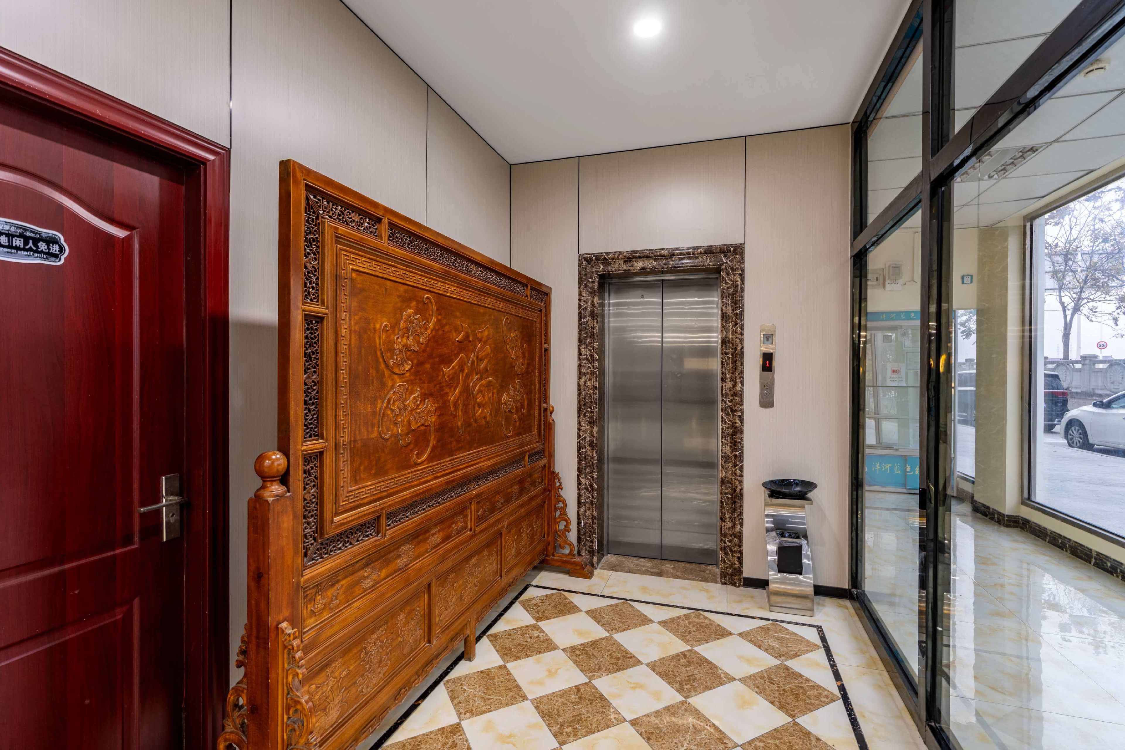 Um saguão de hotel com piso xadrez, balcão de recepção de madeira, elevador e entrada de vidro.