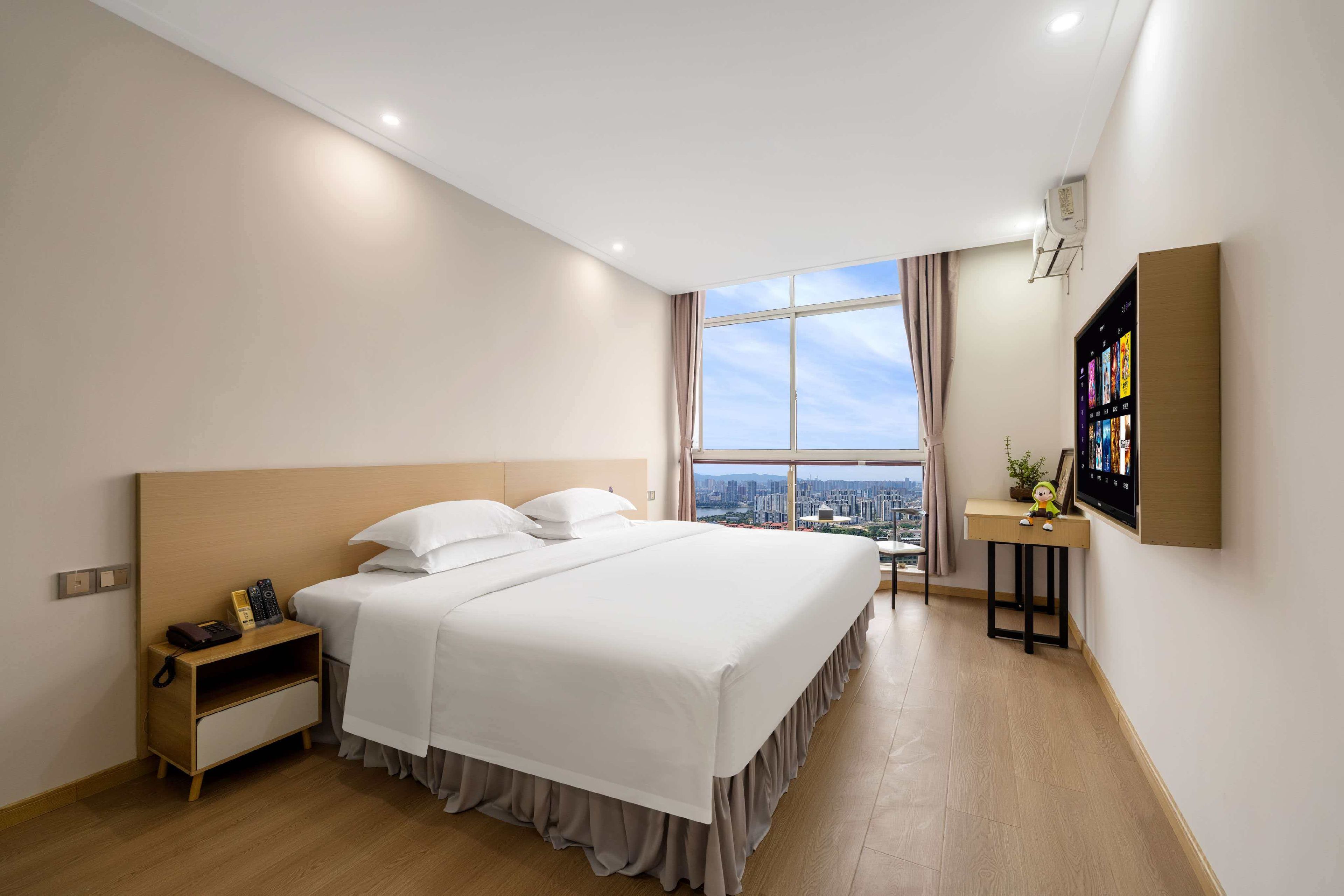 Ein Hotelzimmer mit einem großen Bett, einem Schreibtisch, einem Fernseher und Blick auf die Stadt.