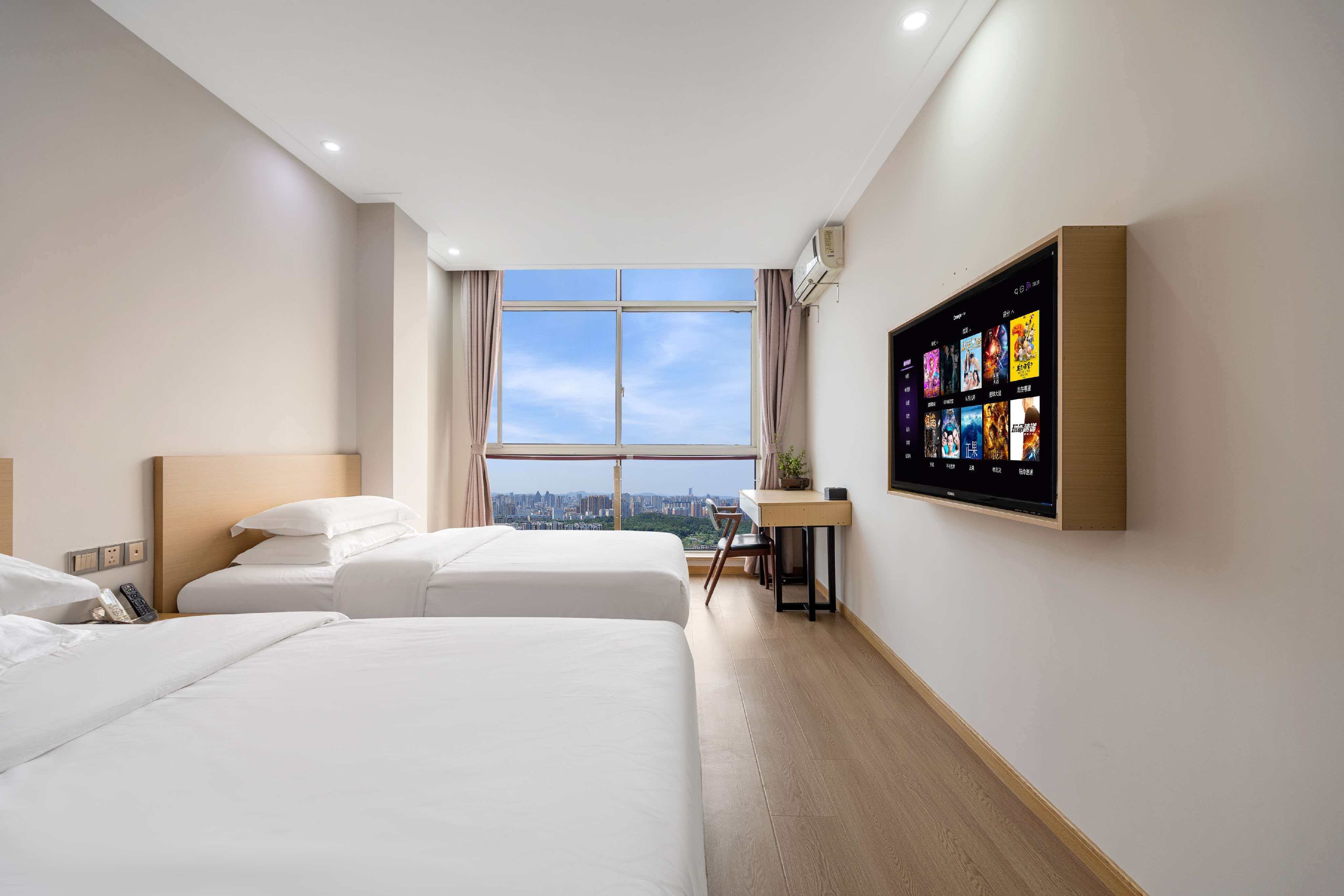 Ein Hotelzimmer mit zwei Betten, einem Schreibtisch, einem Fernseher und Blick auf die Stadt.