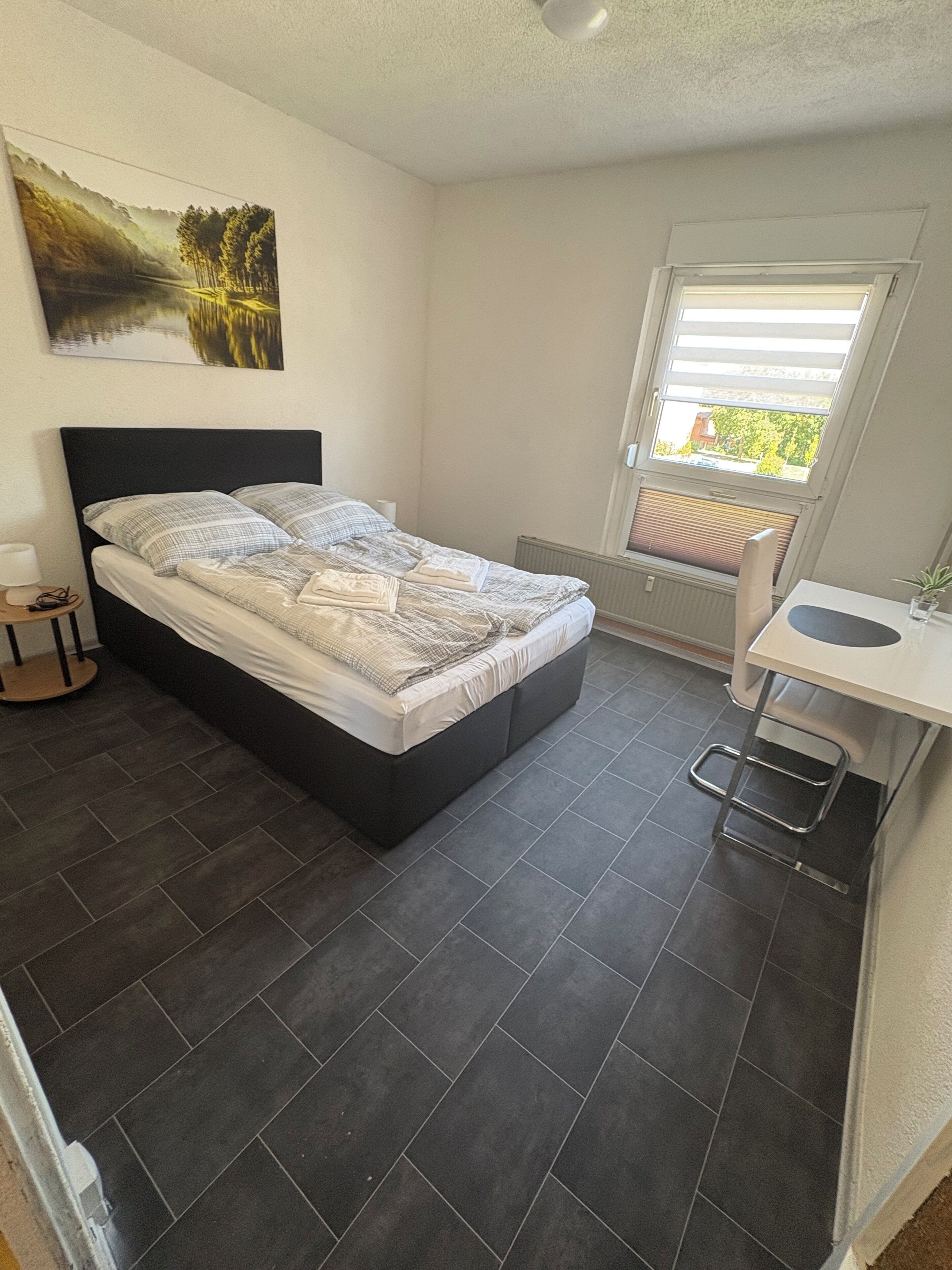 Une chambre à coucher avec un lit, un bureau, une chaise, un radiateur et une fenêtre.