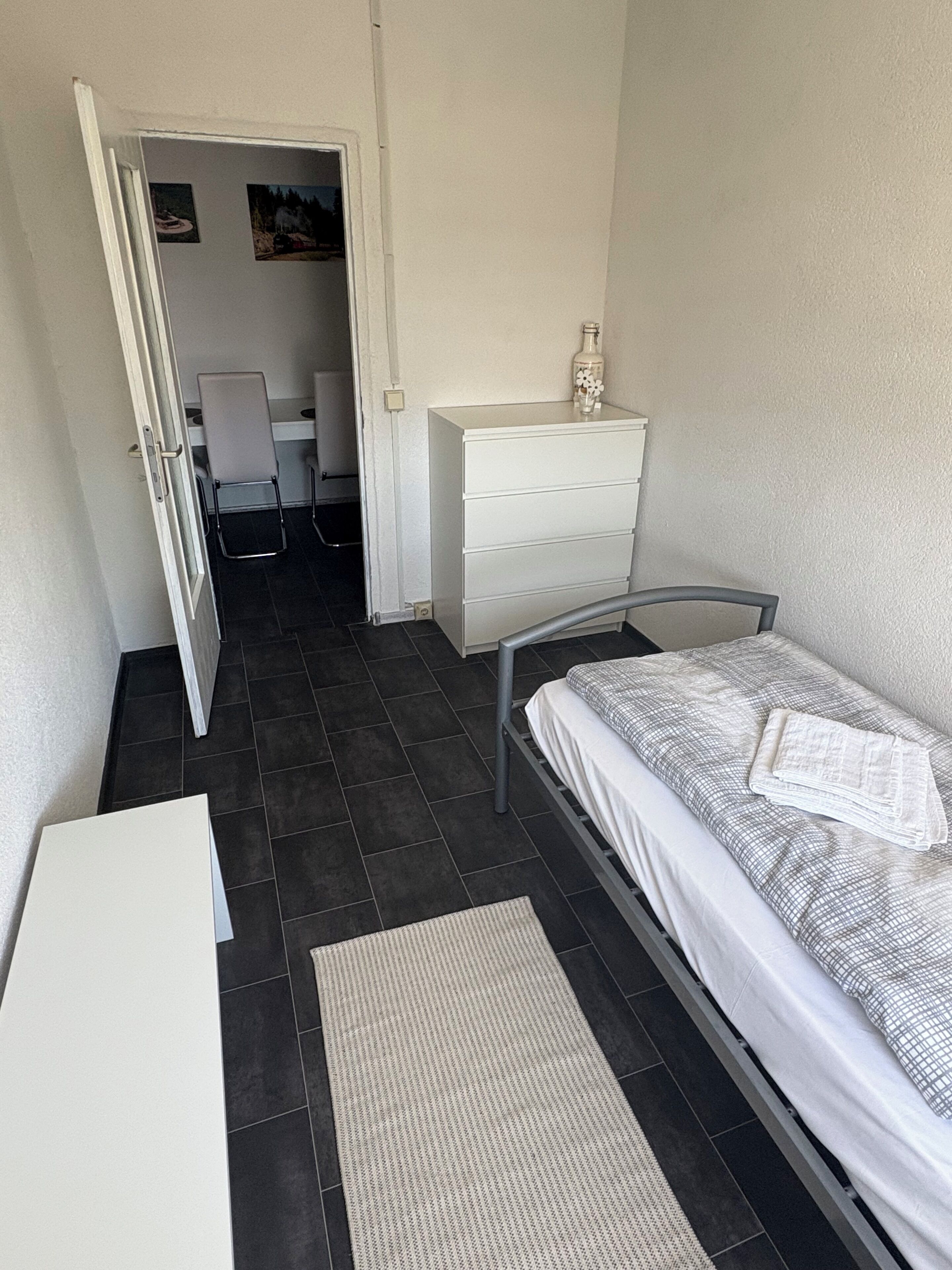 Un dormitorio pequeño y ordenado con una cama, un tocador blanco, un escritorio y una silla.