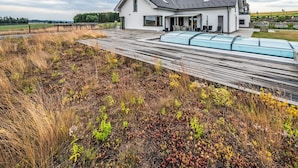 A modern house with a sloped roof, a covered patio, and a garden with wildflowers.