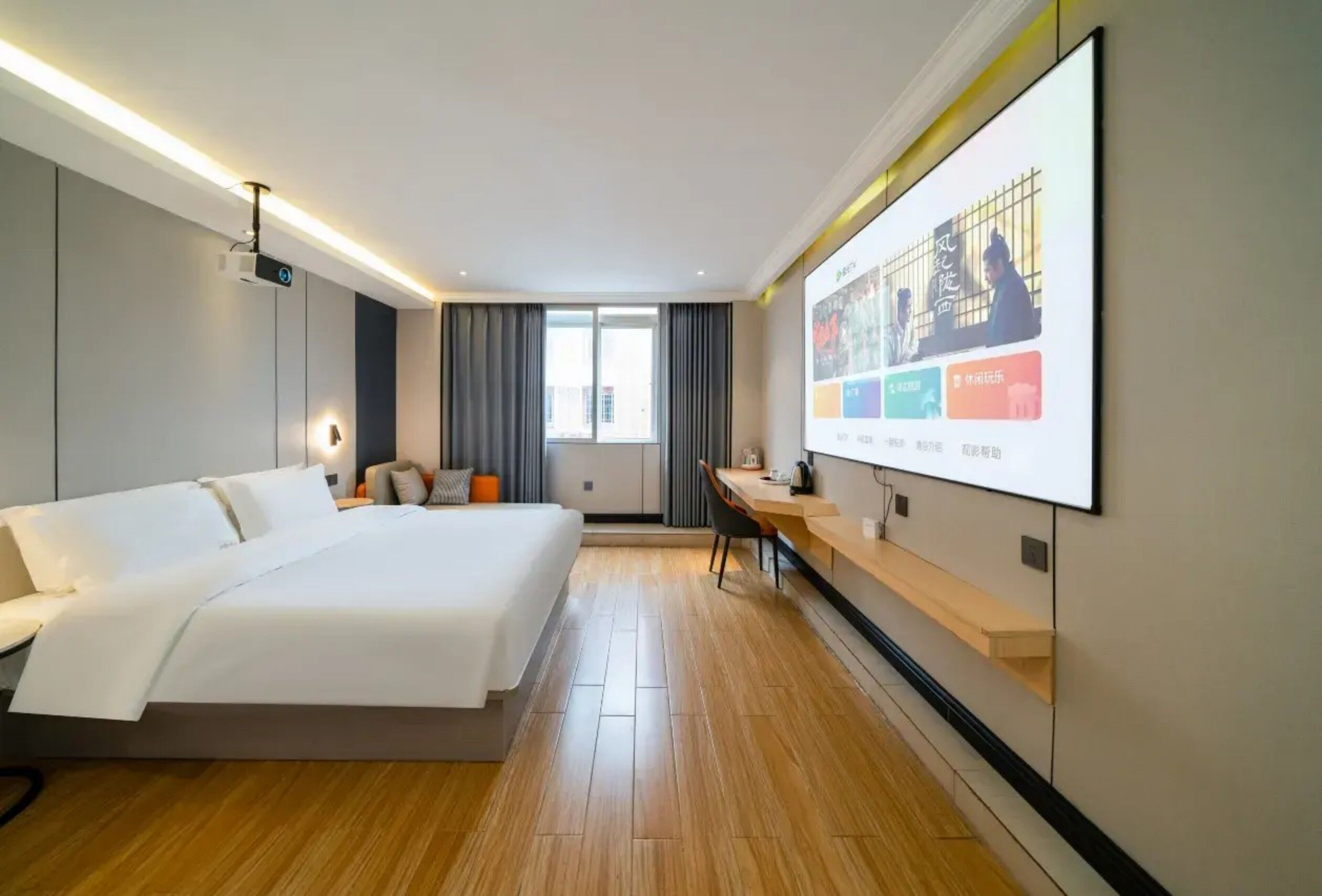 A modern hotel room with a large bed, a desk, a projector screen, and a large window.