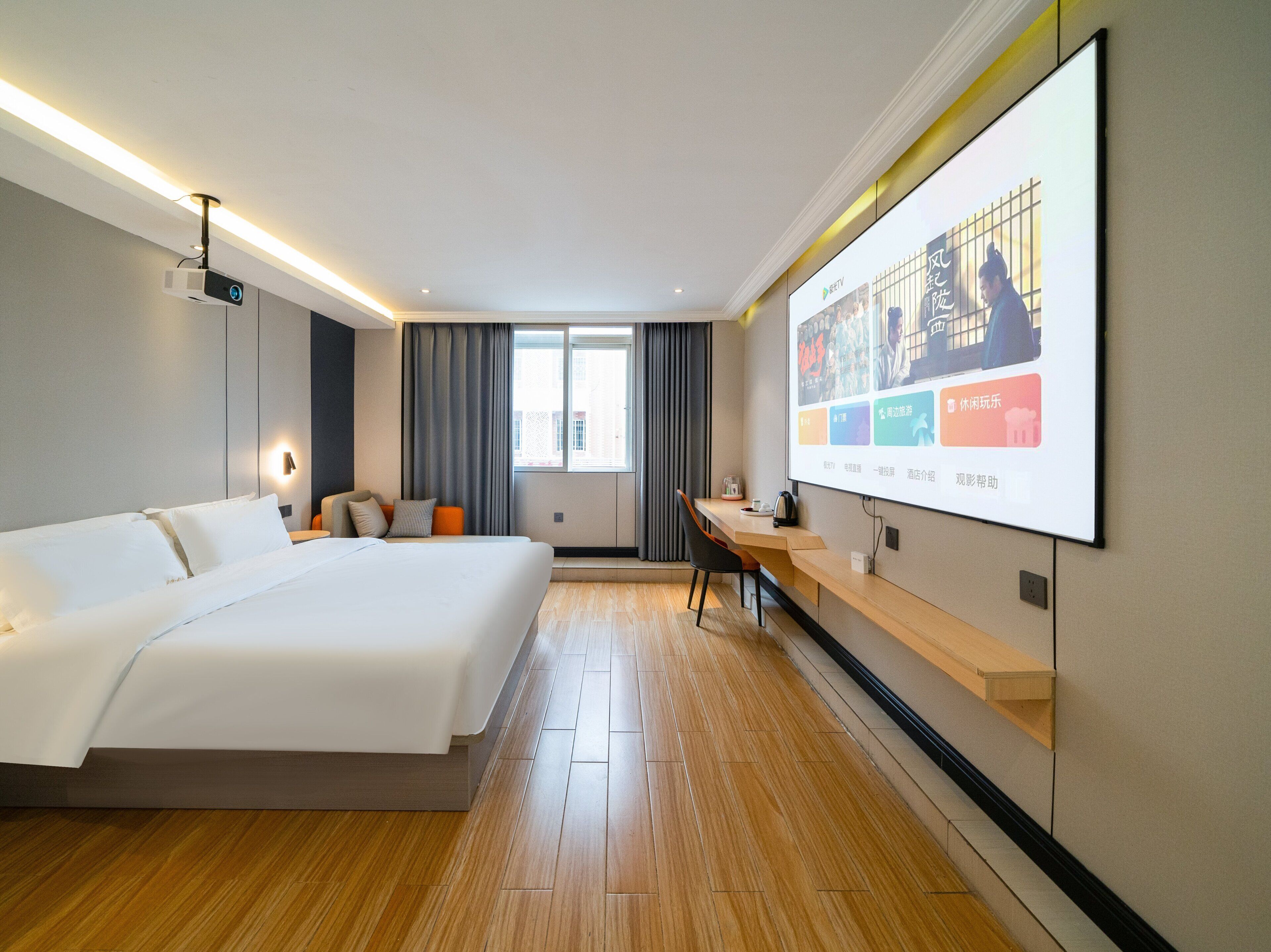 A hotel room with a large bed, a desk, a projector screen displaying a presentation, and a window with curtains.