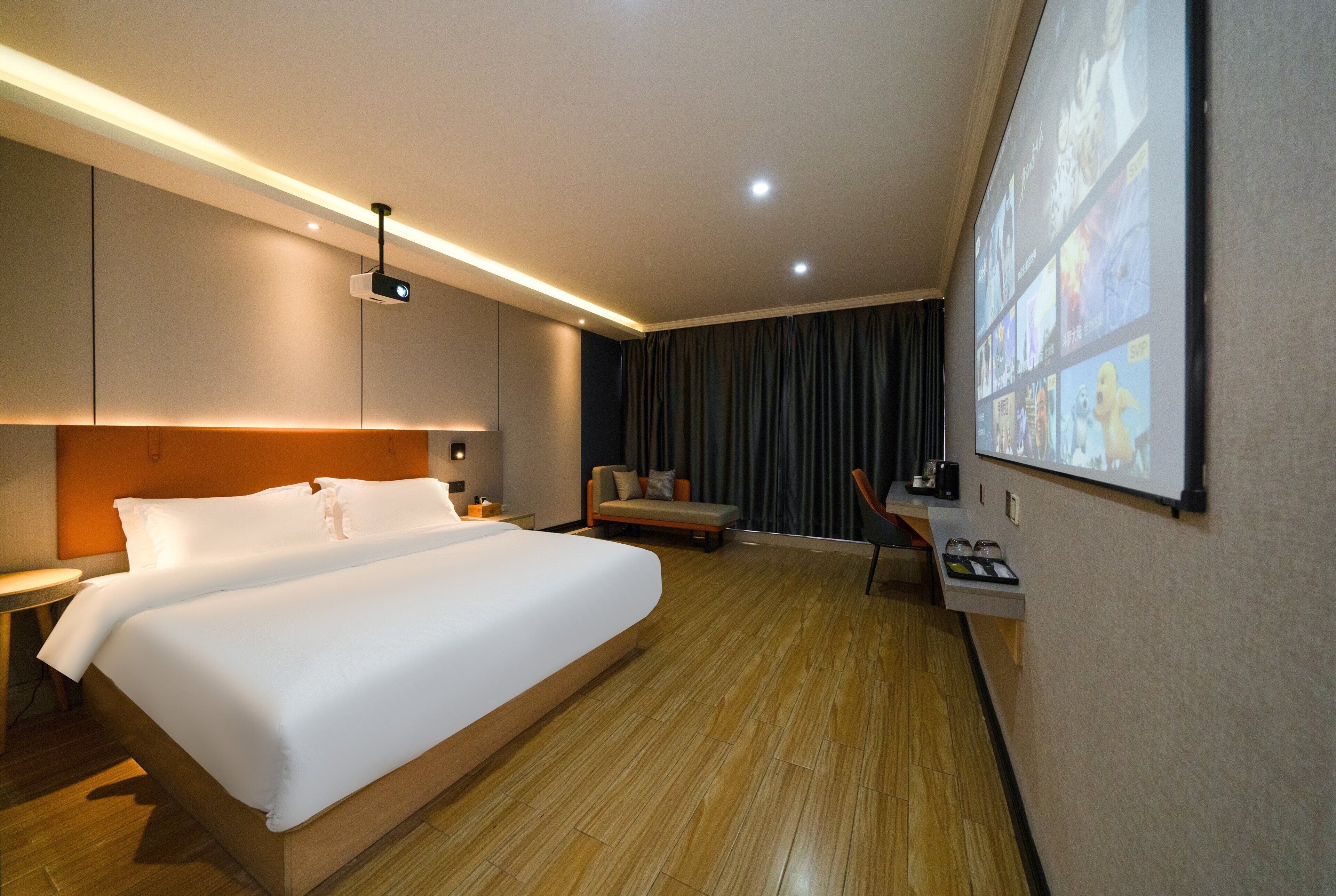 A hotel room with a large bed, a desk, a chair, a projector screen, and a wall-mounted TV.