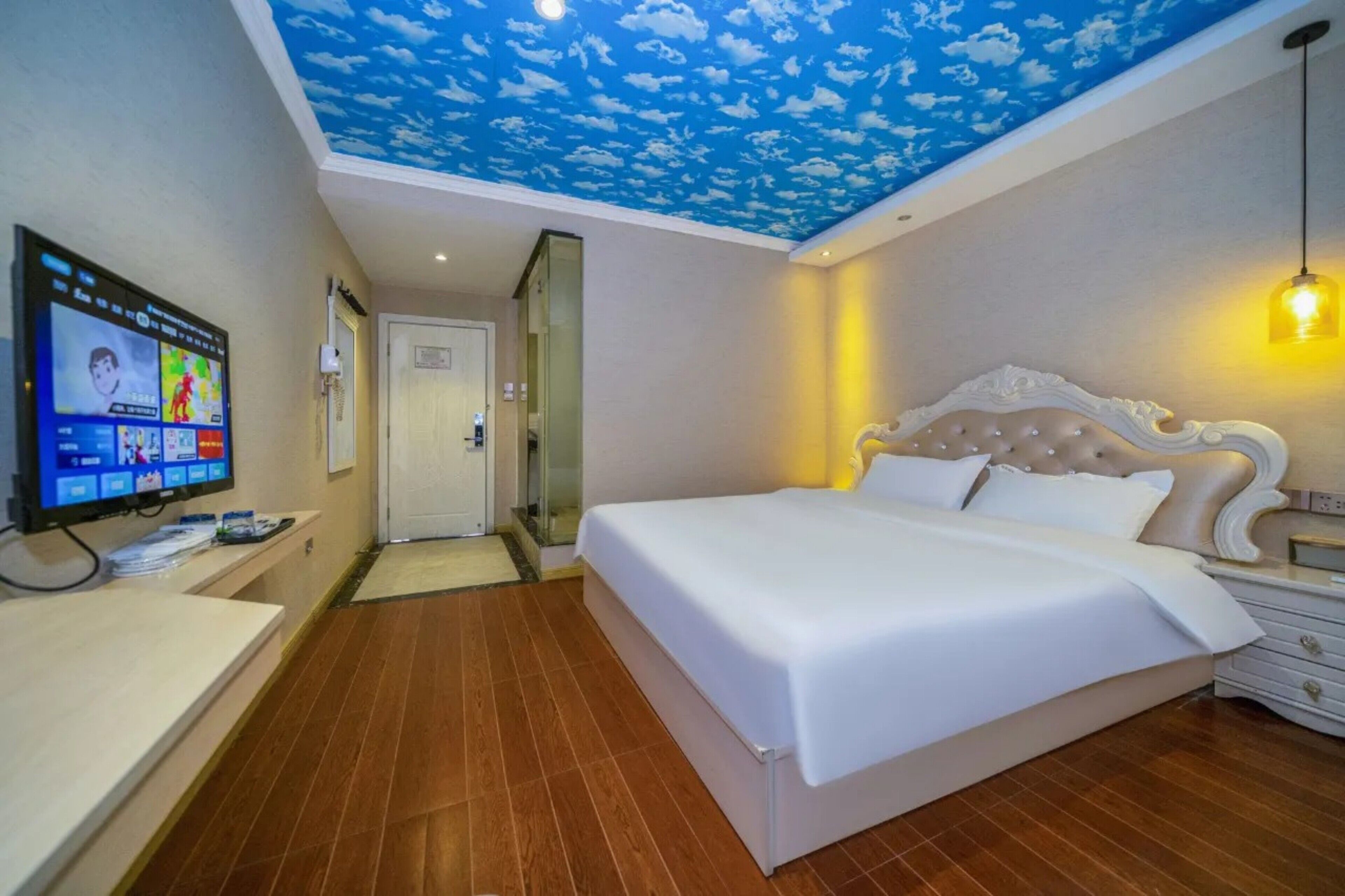 Habitació d'hotel amb llit, televisió, escriptori i sostre amb un disseny de núvols.