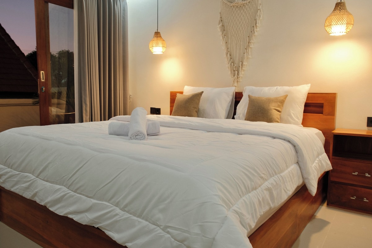 A neatly made bed with white linens, a wooden headboard, and two bedside tables with lamps.
