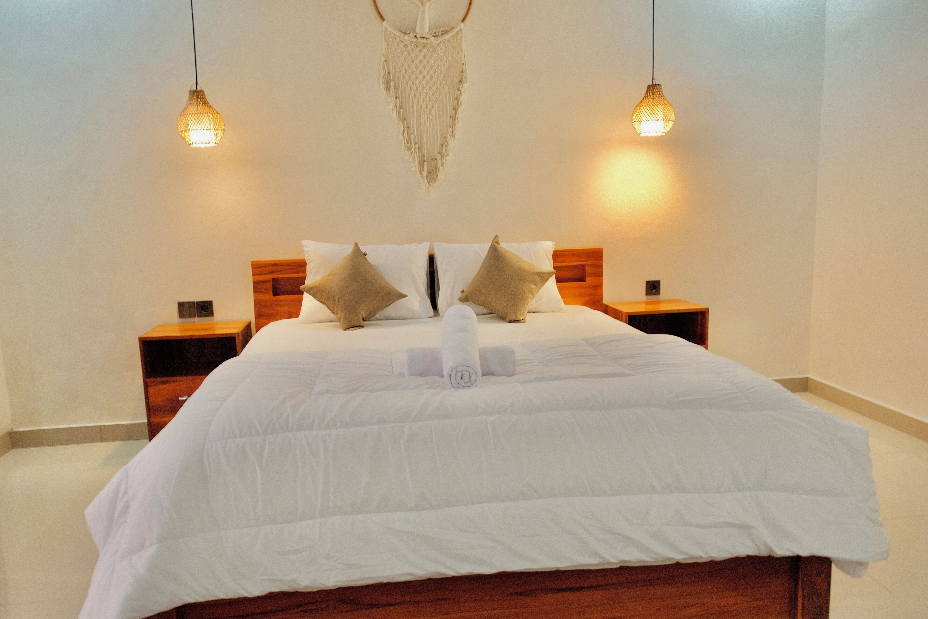 A neatly made bed with white bedding, two wooden nightstands, and hanging macrame light fixtures.