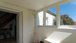 A room with a white exterior wall, a wooden chair, a coat rack, and a window with a view of trees. - Strathnoon by Interhome (Tomatin)